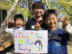 three young boys holding a colorful thank you sign for their teacher