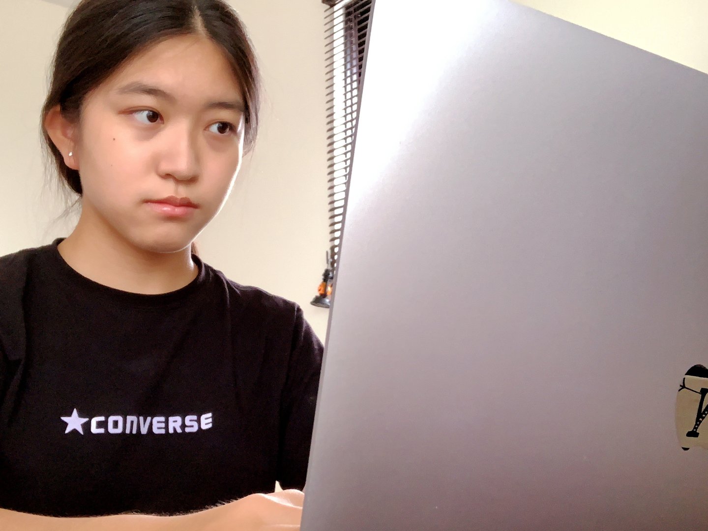 A young Chinese-Japanese girl sits with a determined look in front of her laptop computer.