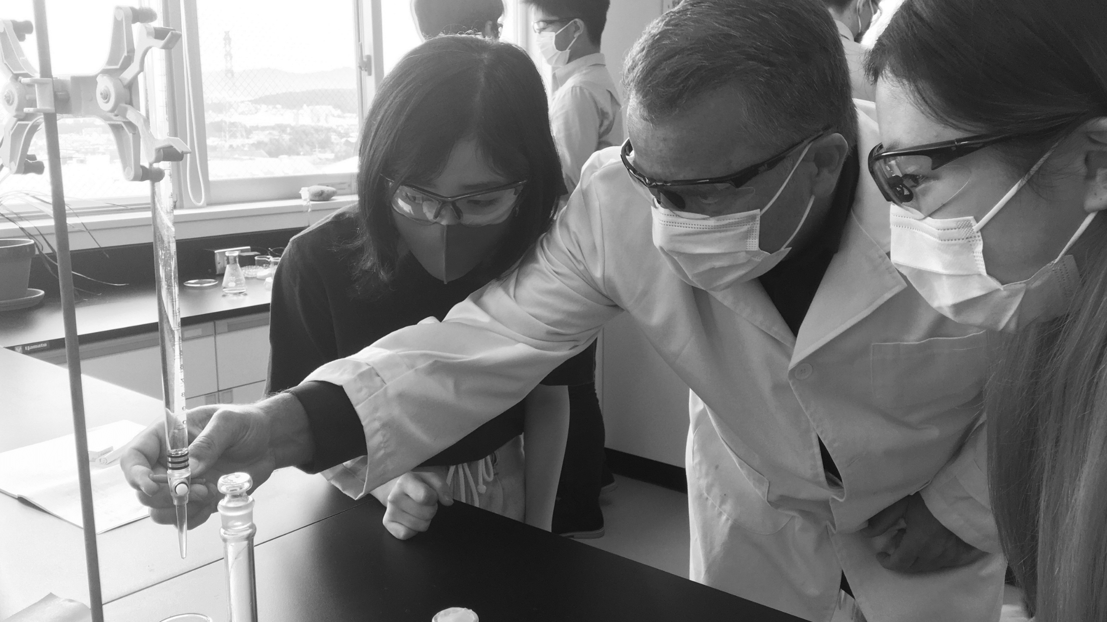 Science teacher is instructing two girls how to pipette some liquid.