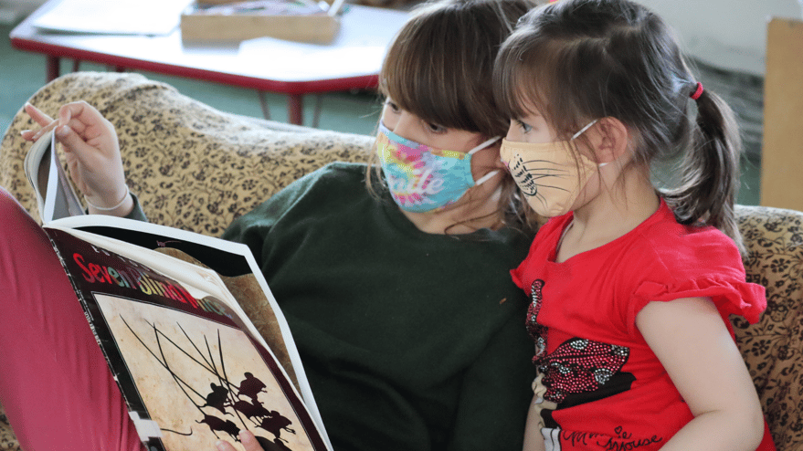 Two girls sitting on a sofa reading a picture book.