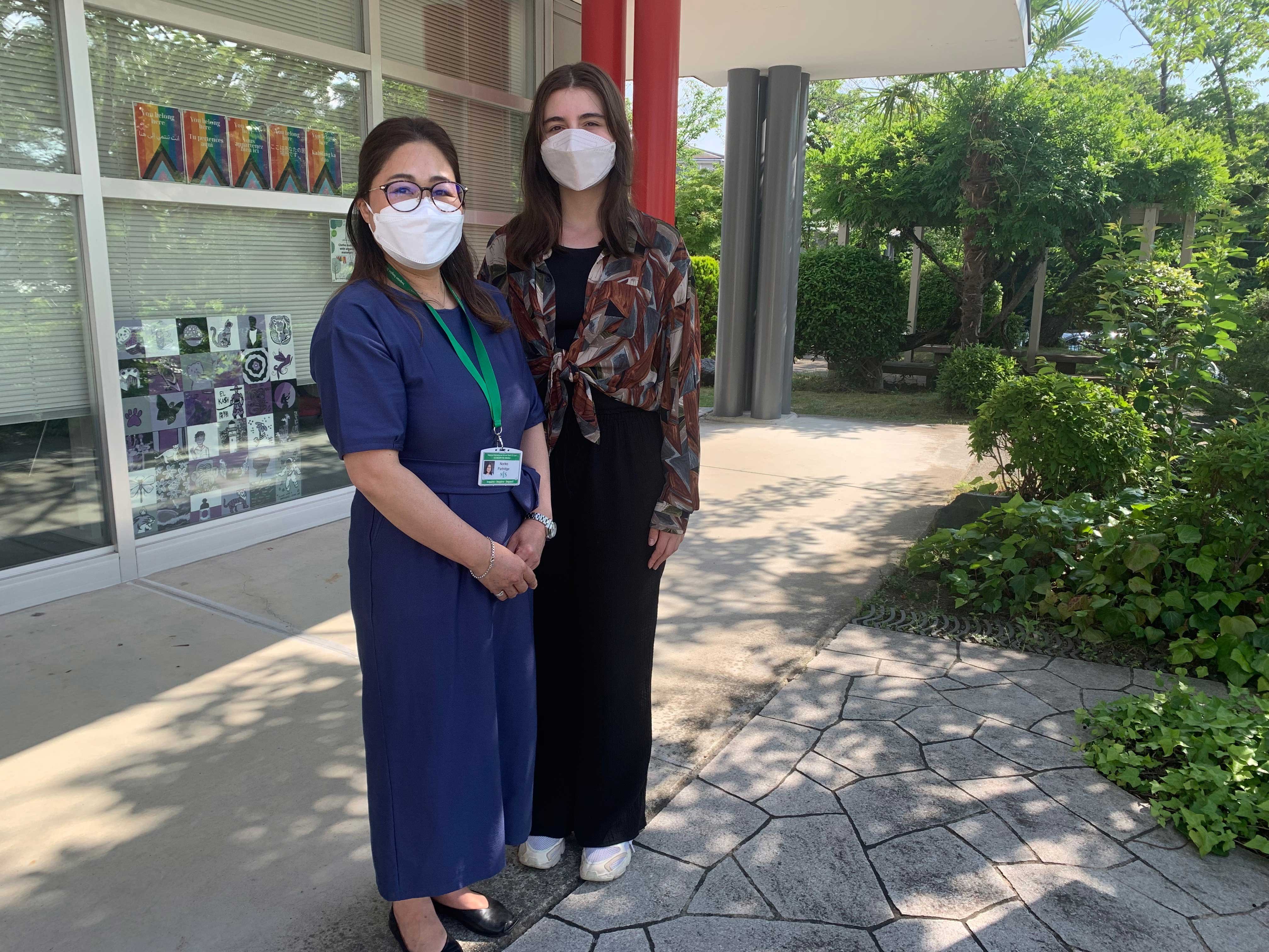 A student and her teacher stand in the school courtyard.