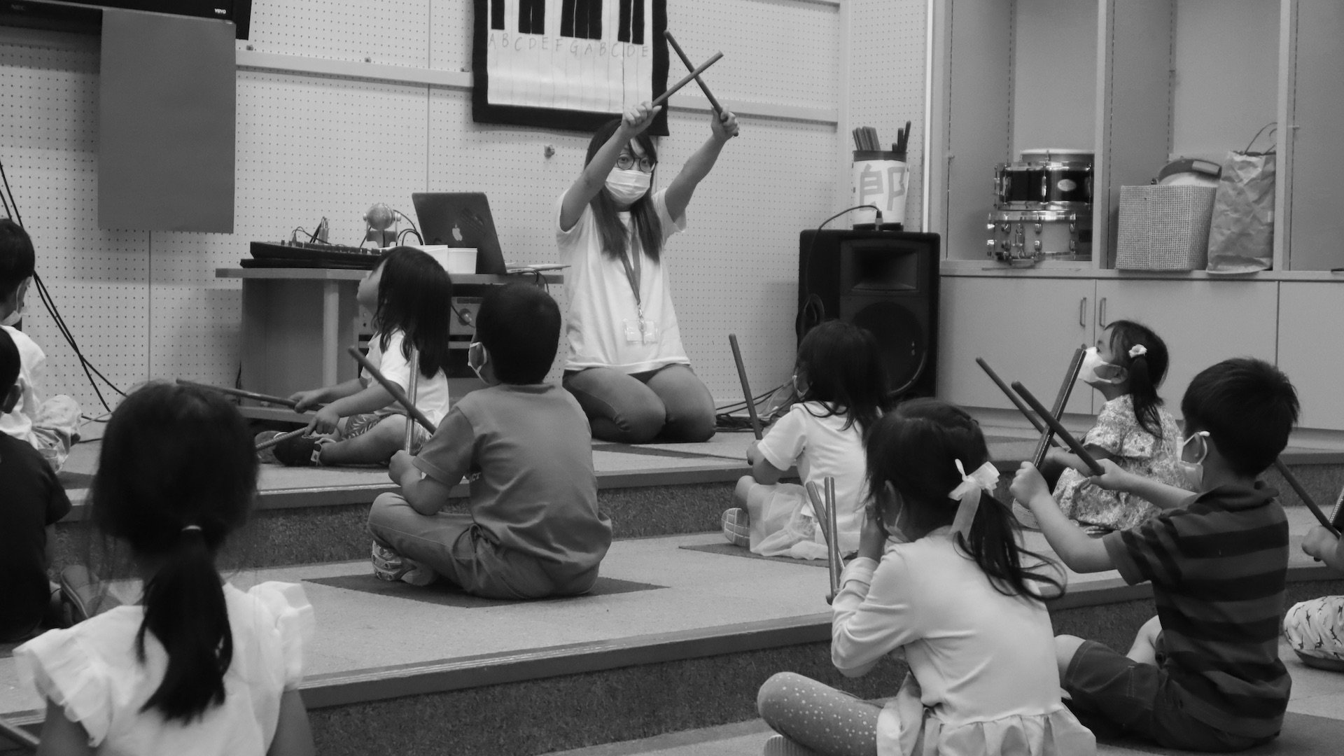 A teacher is instructing young students to create music with sticks.