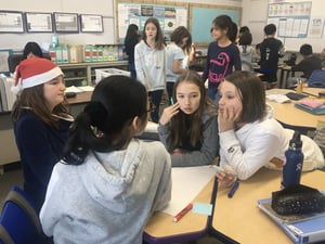 Four elementary girls sitting at desks in a group discussing their school project.