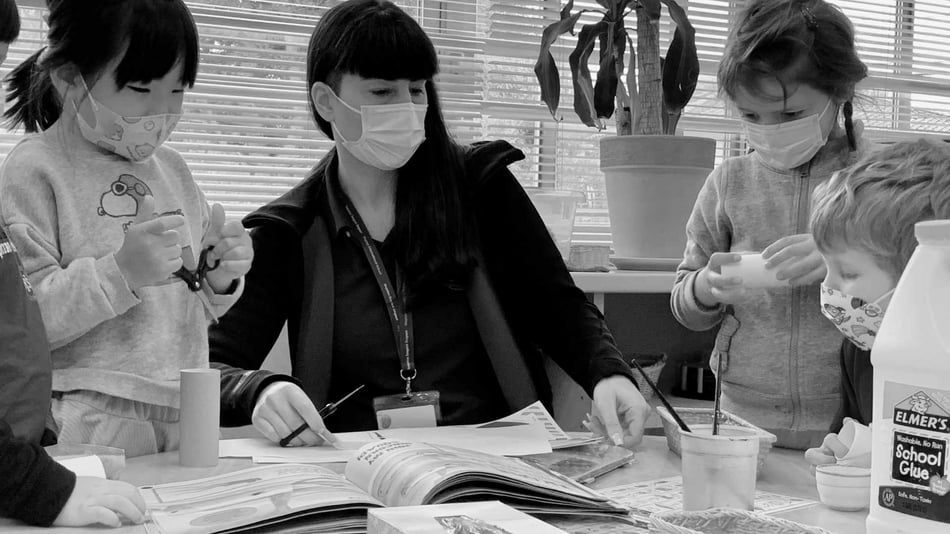 A teacher is sitting at a table doing an art project with pre-school children.