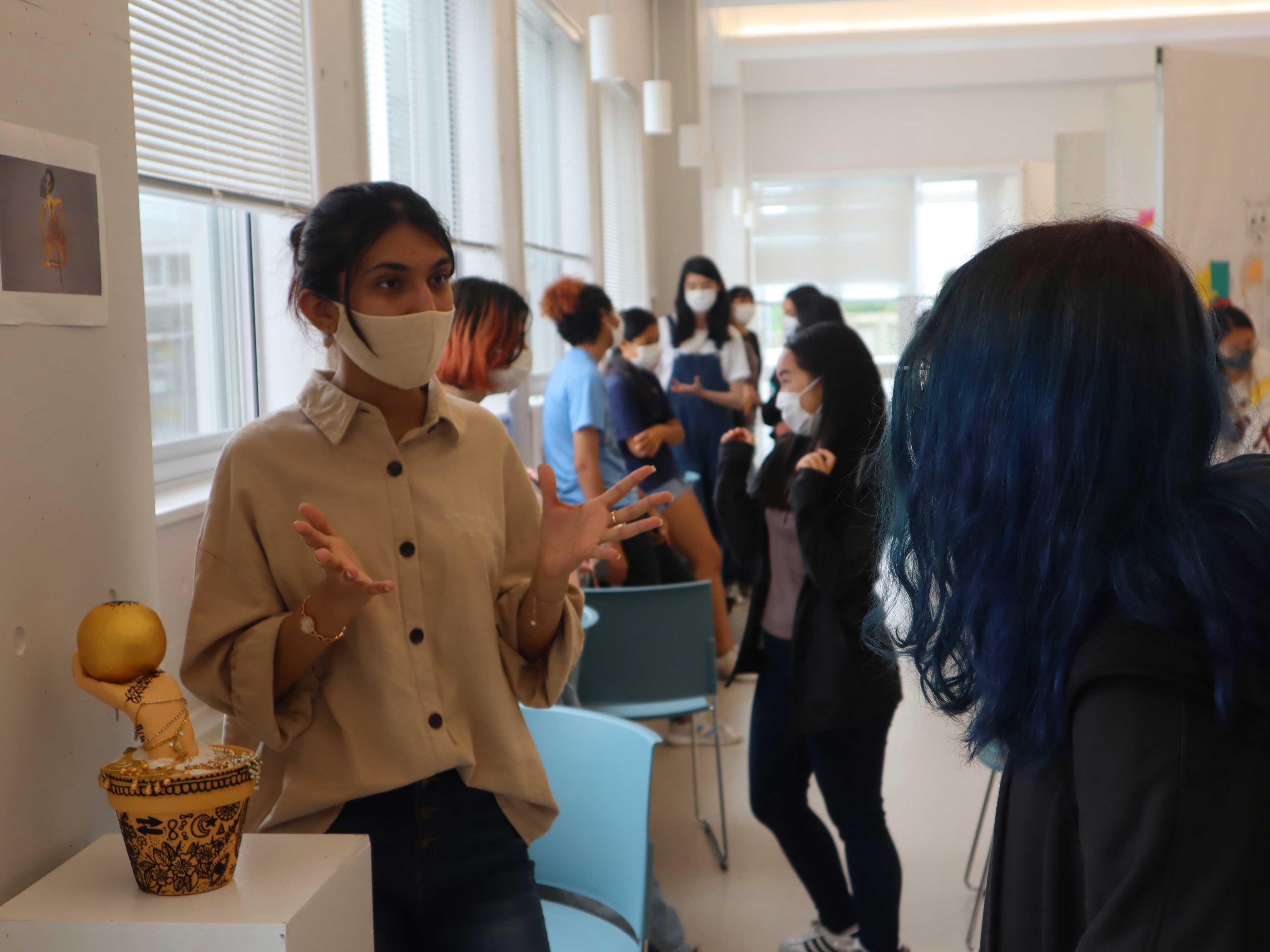 A female student explains to another female student about her her Theory of Knowledge entry into the TOK exhibit.