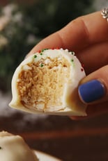 A hand holding a homemade peanut butter cookie covered with white chocolate and red and green decorations.