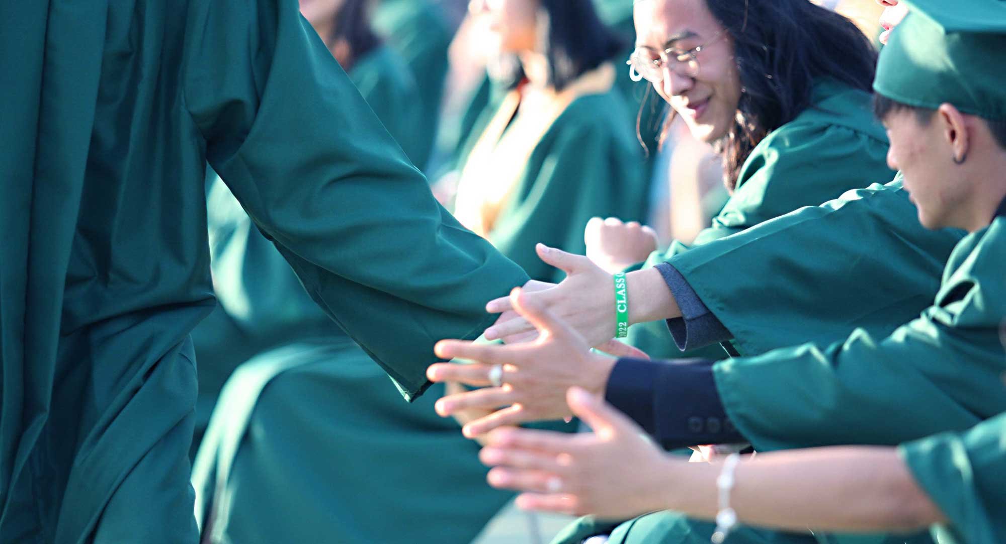 Graduates of the class of 2020 slap hands in congratulations.