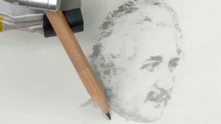 A robotic arm holds a pencil and is sketching a picture of Einstein using dark and light shading.